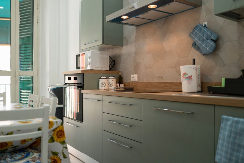 A kitchen with a microwave, toaster, and a refrigerator. There is a window with blinds and a table with chairs.