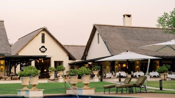 A poolside area with outdoor seating and a building with a thatched roof. - Livingstone junior s (Livingstone)