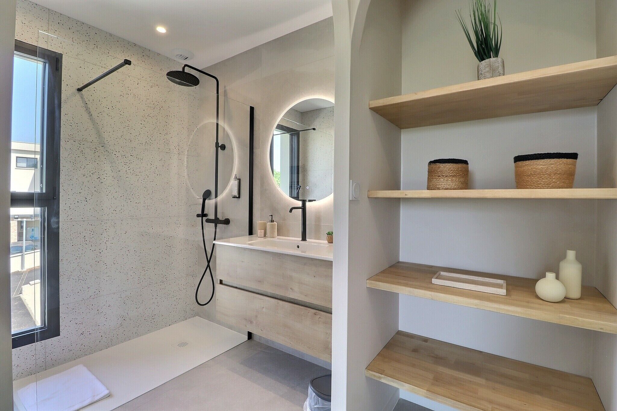 Une salle de bain moderne avec une baignoire sur pieds, un grand miroir et des étagères en bois ornées d’objets décoratifs.
