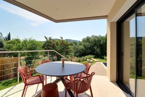 A covered outdoor patio with a round table and chairs, a pool, and a view of a garden and hills. - Villa Nova (Ventabren)