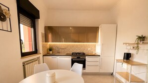 A compact kitchen with a round dining table, white chairs, a built-in stove, and a refrigerator. - At Cherie's House! Nettuno! (Nettuno)