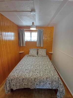 A single bed with a patterned bedspread in a room with wooden walls and a white ceiling. - Just like home: a cozy apartment with a local host (Talmont-Saint-Hilaire)