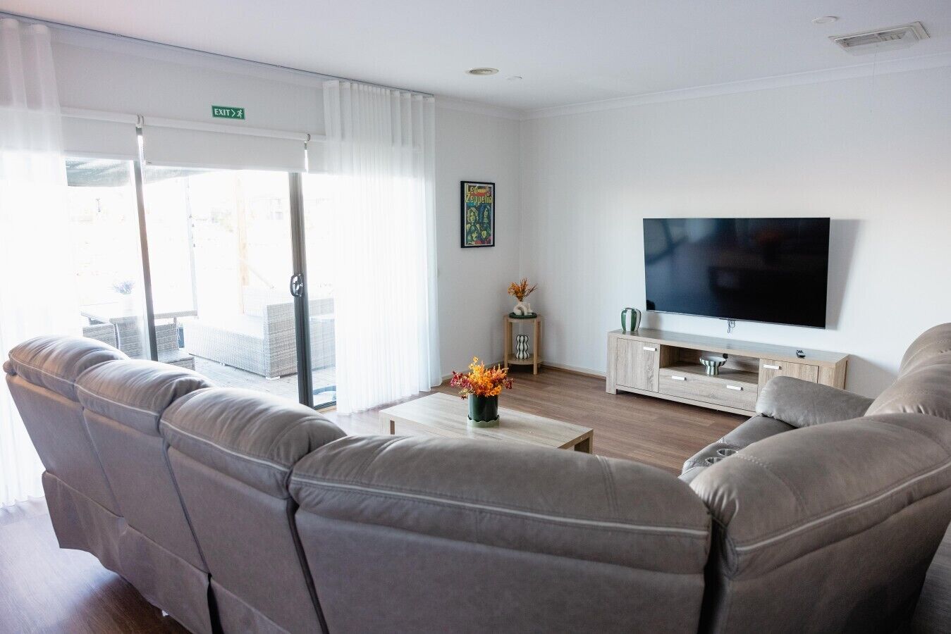 A modern living room with a sofa set, a flat-screen TV, and a small side table with a vase of flowers.