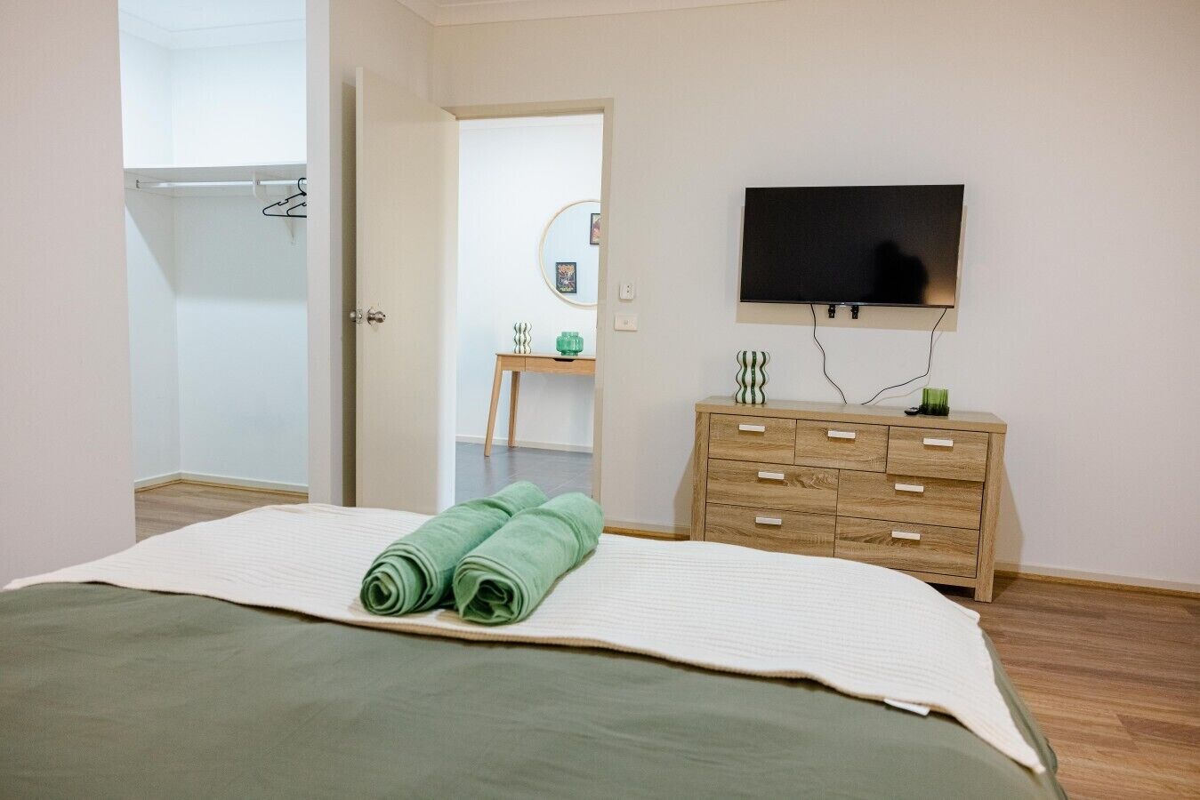 A bedroom with a bed, a dresser, a television, and a door leading to another room.
