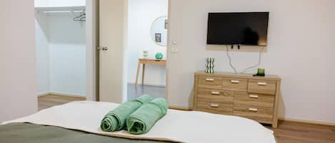 Un dormitorio con cama, cómoda, televisor y puerta que da a otra habitación.