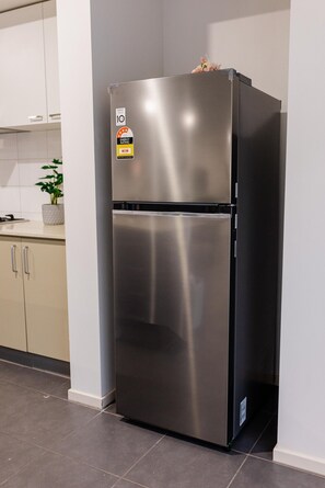 Ein Edelstahl-Kühlschrank in einer Küche mit weißen Schränken und Fliesenboden.