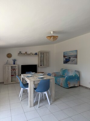 A dining area with a table set for four, a sofa, and a television. - Blue House - Panoramic View of the Gulf of Asinara (Sardegna)