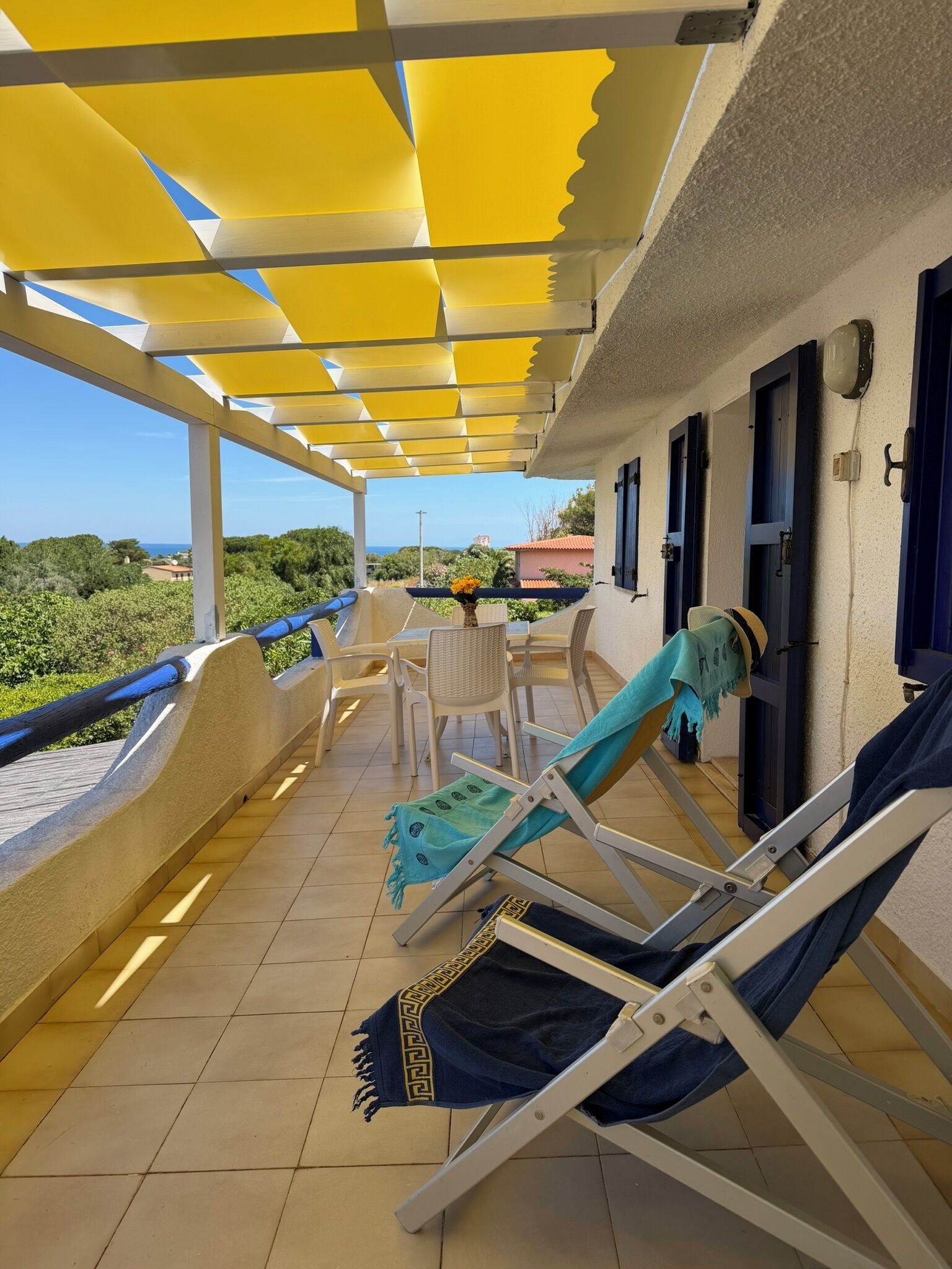 A covered outdoor seating area with lounge chairs and a table, overlooking a scenic view.