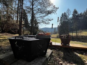 An outdoor grill with a basket and a plate of food, set against a backdrop of trees and a clear sky.