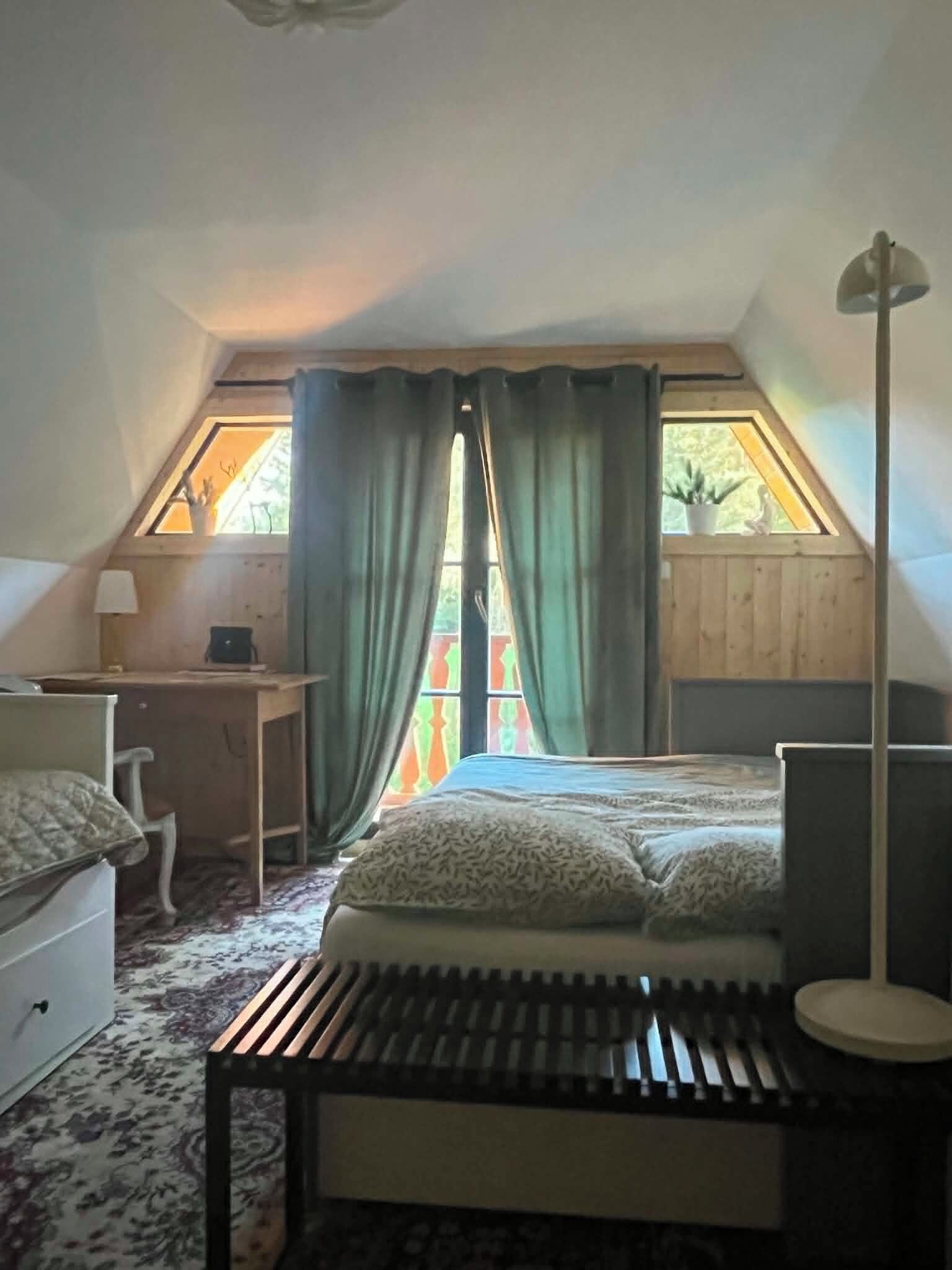 A bedroom with a sloped ceiling, a bed, a desk, a chair, and a floor lamp.