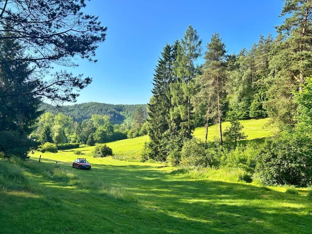 A car parked on a grassy field with trees and hills in the background.
