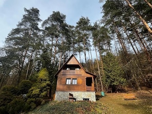 Eine Holzhütte mit einem Balkon, umgeben von dichtem Wald.