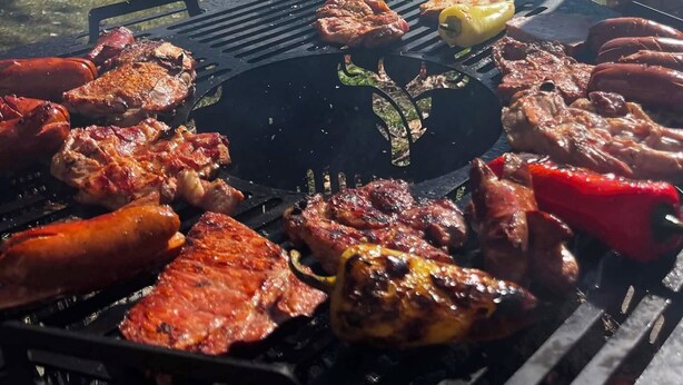 Una parrilla al aire libre con diversos tipos de carne y verduras asándose.