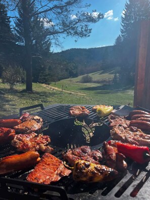 Una parrilla al aire libre con diversos tipos de carne y verduras asándose.