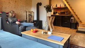Una sala de estar acogedora con chimenea, un comedor con una mesa dispuesta para dos personas, y una cocina visible a través de un umbral abierto.