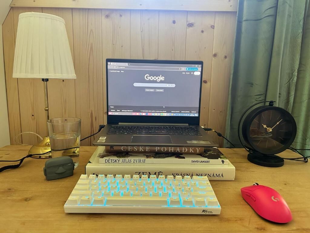 En bärbar dator står på ett skrivbord i trä, tillsammans med ett tangentbord, en mus och några böcker.