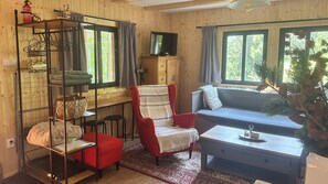 A cozy cabin interior with a red armchair, a blue sofa, a wooden TV stand, and a shelf with towels and baskets. - Chata za dubem (Všelibice)
