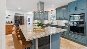 A modern kitchen with a central island, stainless steel appliances, and teal cabinetry. - Game Room | Open Living Space | Large Kitchen | Sunroom | Fenced Backyard | Fire Pit (St. Simons Island)
