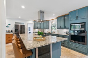 A modern kitchen with a central island, stainless steel appliances, and teal cabinetry. - Game Room | Open Living Space | Large Kitchen | Sunroom | Fenced Backyard | Fire Pit (St. Simons Island)