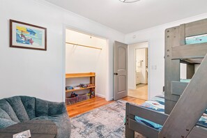 Ein Zimmer mit einem Etagenbett, einem Sessel, einem gerahmten Bild und einem Holzregal mit diversen Gegenständen.