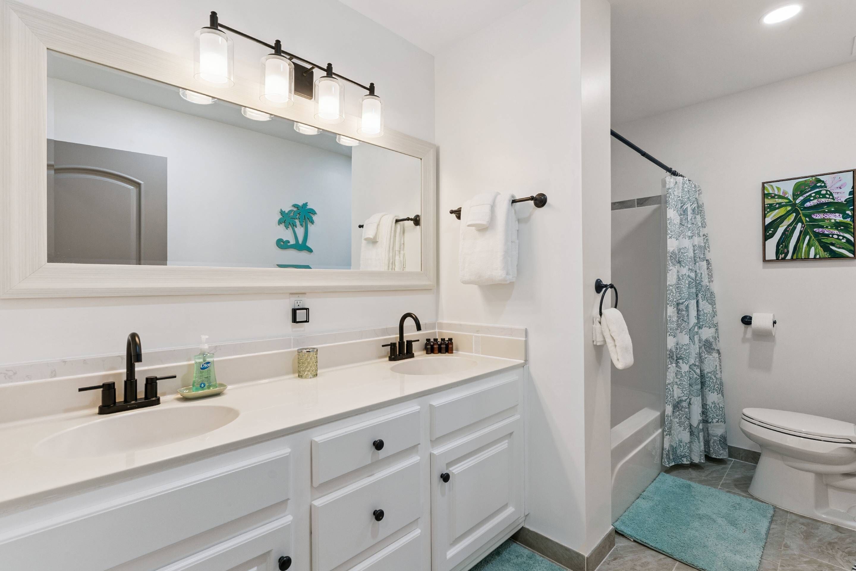 A bathroom with a white vanity, a mirror, a sink, a toilet, and a shower curtain.