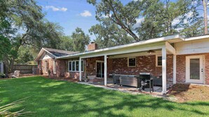 A brick house with a covered patio, a grill, and a lawn. - Game Room | Open Living Space | Large Kitchen | Sunroom | Fenced Backyard | Fire Pit (St. Simons Island)