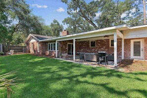 A brick house with a covered patio, a grill, and a lawn. - Game Room | Open Living Space | Large Kitchen | Sunroom | Fenced Backyard | Fire Pit (St. Simons Island)