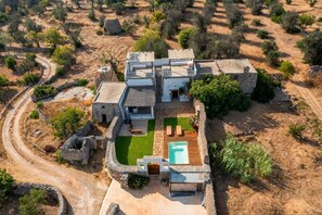 Een moderne villa met zwembad, gelegen in een droog landschap met schaarse begroeiing.