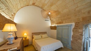 Ein Schlafzimmer mit einem Bett, Nachttischlampen, einem Beistelltisch, einem hölzernen Kopfteil, einer Tür und einer Steinwand.