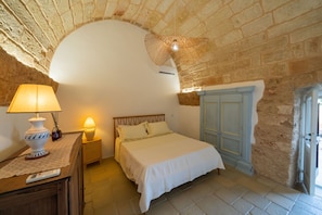 Ein Schlafzimmer mit einem Bett, Nachttischlampen, einem Beistelltisch, einem hölzernen Kopfteil, einer Tür und einer Steinwand.