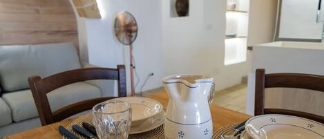 Una mesa de comedor con una jarra, platos y cubiertos, en una habitación con techo de madera y un sofá.