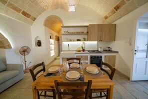 A cozy kitchen with a dining table set for four, a fan, and a stone archway. - A little gem: ancient country house with pool (Leuca)