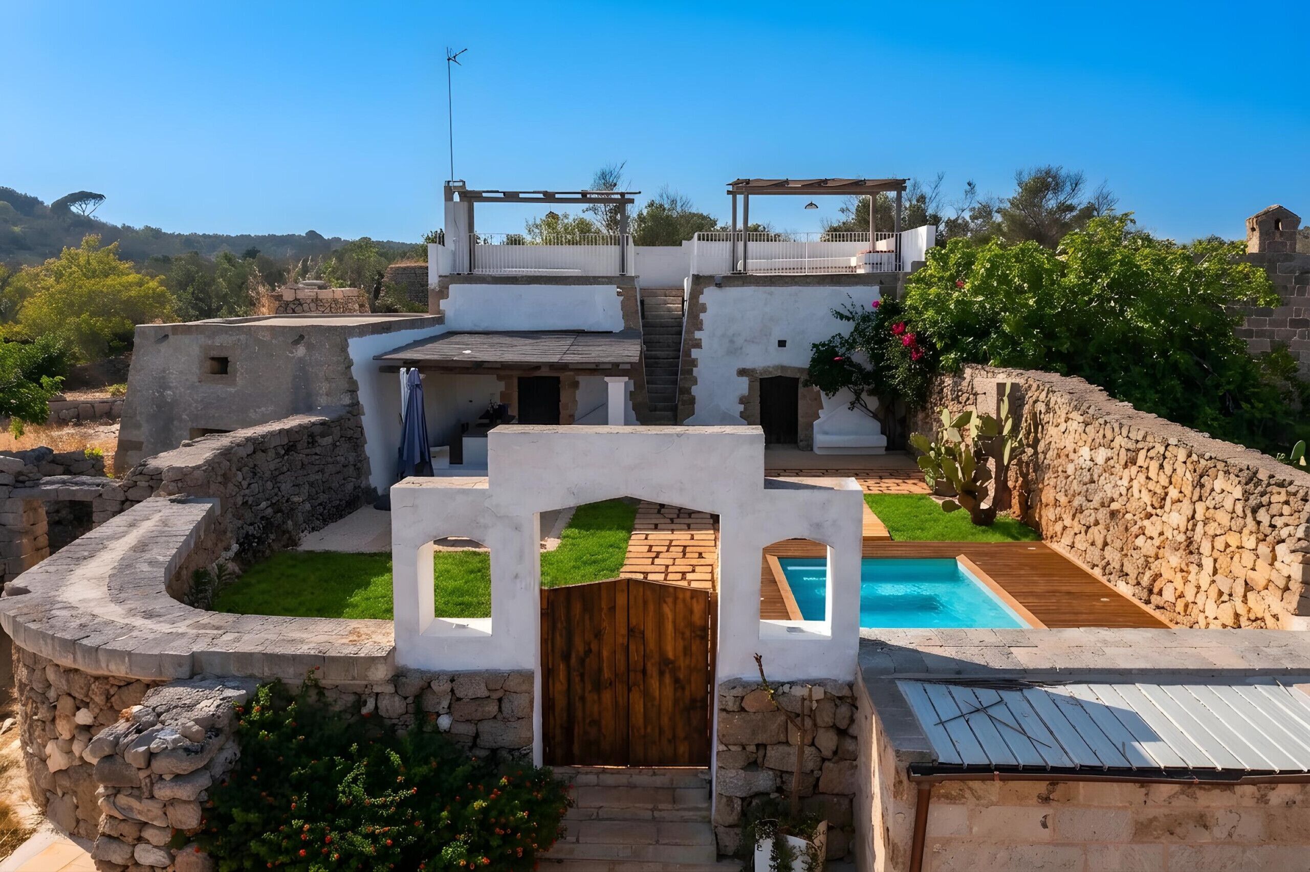 Una villa con piscina, muros de piedra y puerta de madera.