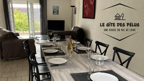 Un'area pranzo con un tavolo lungo apparecchiato per sei persone, sedie, una televisione e una parete con un logo e del testo.