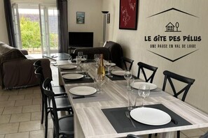 A dining area with a long table set for six, chairs, a TV, and a wall with a logo and text. - The Gîte des Pélus, perfect for a getaway in the countryside, less than 10 minutes from Tours. (Rochecorbon)
