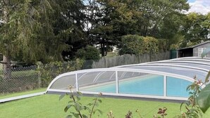 Una piscina con un recinto in vetro curvo, circondata da un prato e da una recinzione in legno.