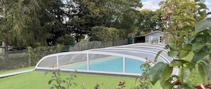 A swimming pool with a curved glass enclosure, surrounded by a grassy yard and a wooden fence. - The Gîte des Pélus, perfect for a getaway in the countryside, less than 10 minutes from Tours. (Rochecorbon)