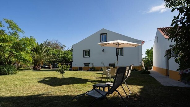 Un edificio blanco con techo plano, un patio con mesa y sillas, y un césped.