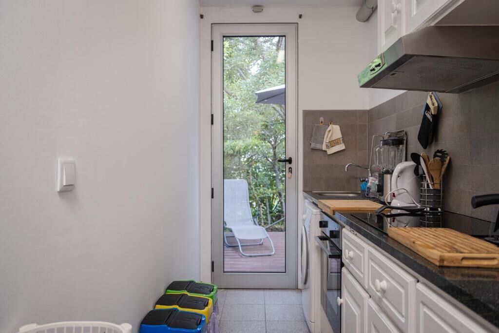 Une cuisine compacte avec une porte donnant sur un balcon, un lave-linge et un plan de travail sur lequel sont disposés divers ustensiles de cuisine.
