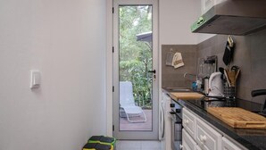 Cocina compacta con acceso a un balcón, lavadora y encimera con diversos utensilios de cocina.