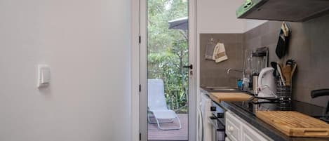 A compact kitchen with a door leading to a balcony, a washing machine, and a countertop with various kitchen items.