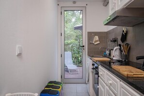A compact kitchen with a door leading to a balcony, a washing machine, and a countertop with various kitchen items. - Quinta de S. Caetano- S. Miguel-Açores (Ponta Delgada)