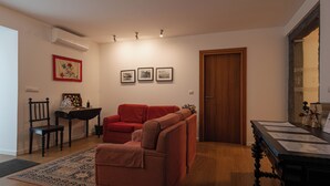 Una sala de estar con un sofá rojo, una silla a rayas, una mesa de centro de madera y una puerta. Hay tres cuadros en la pared.