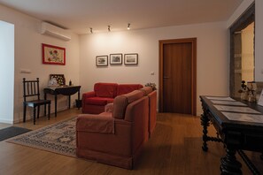 A living room with a red sofa, a striped chair, a wooden coffee table, and a door. There are three framed pictures on the wall. - Quinta de S. Caetano- S. Miguel-Açores (Ponta Delgada)