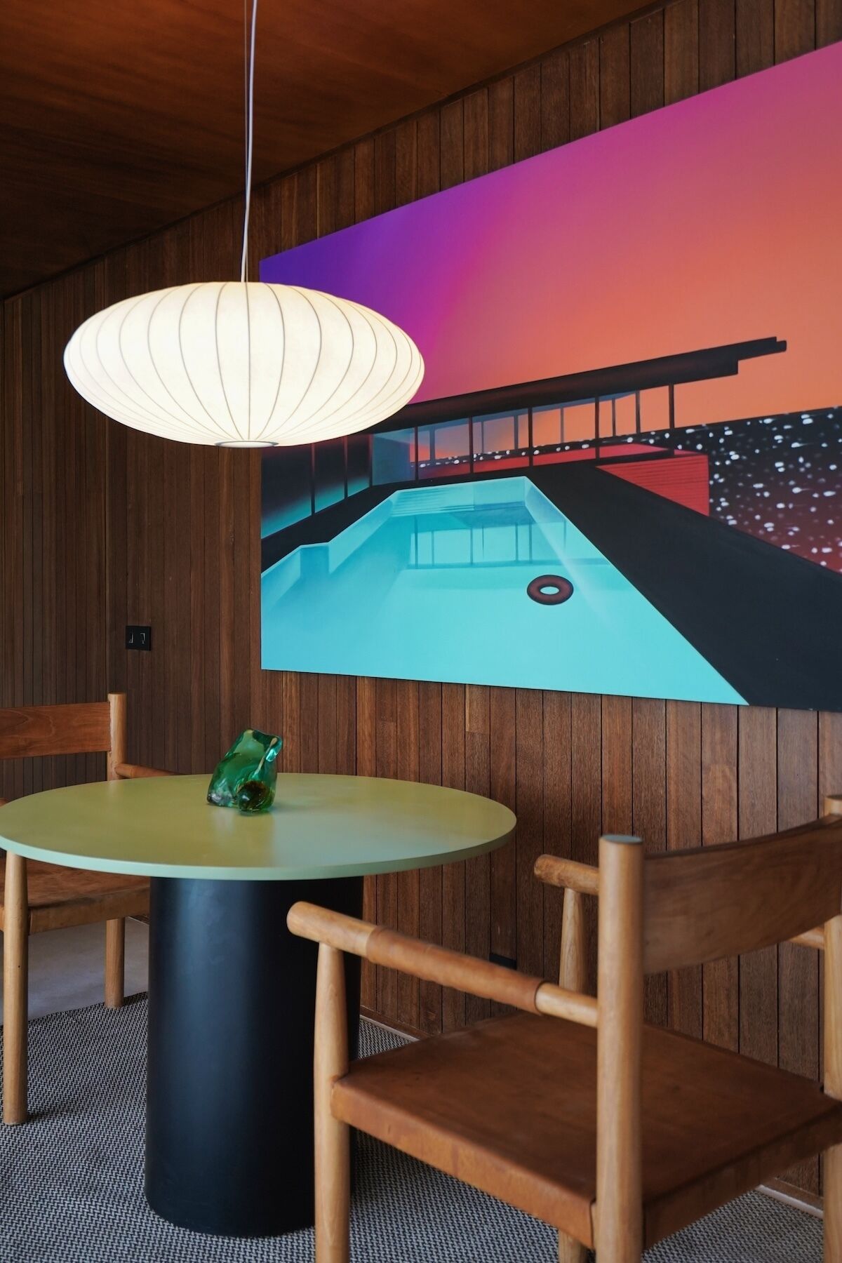 A dining area with a round table, chairs, a hanging light fixture, and a colorful wall mural.