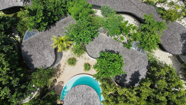 An aerial view of a resort with multiple circular roofed areas, a central swimming pool, and surrounding greenery. - Nya Uluwatu (Pecatu)