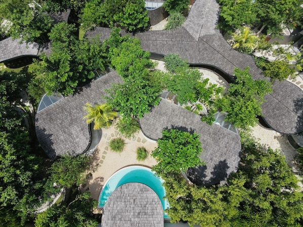 Vista aérea de un resort con varias zonas de techo circular, una piscina central y abundante vegetación.