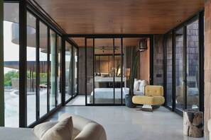 Un dormitorio moderno con un ventanal grande, una cama, un sofá y vistas a una piscina.