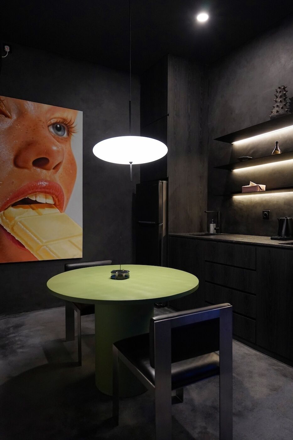 A modern kitchen with a round table, pendant lighting, and a large wall art piece.