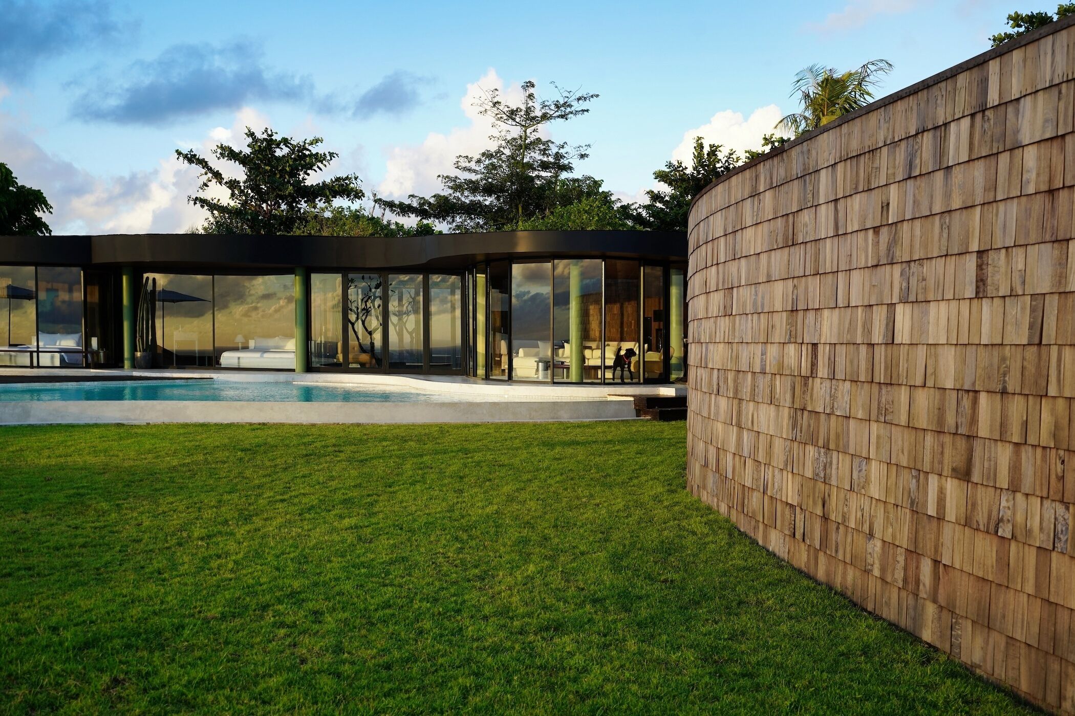 A modern house with a swimming pool, glass walls, and a wooden fence.